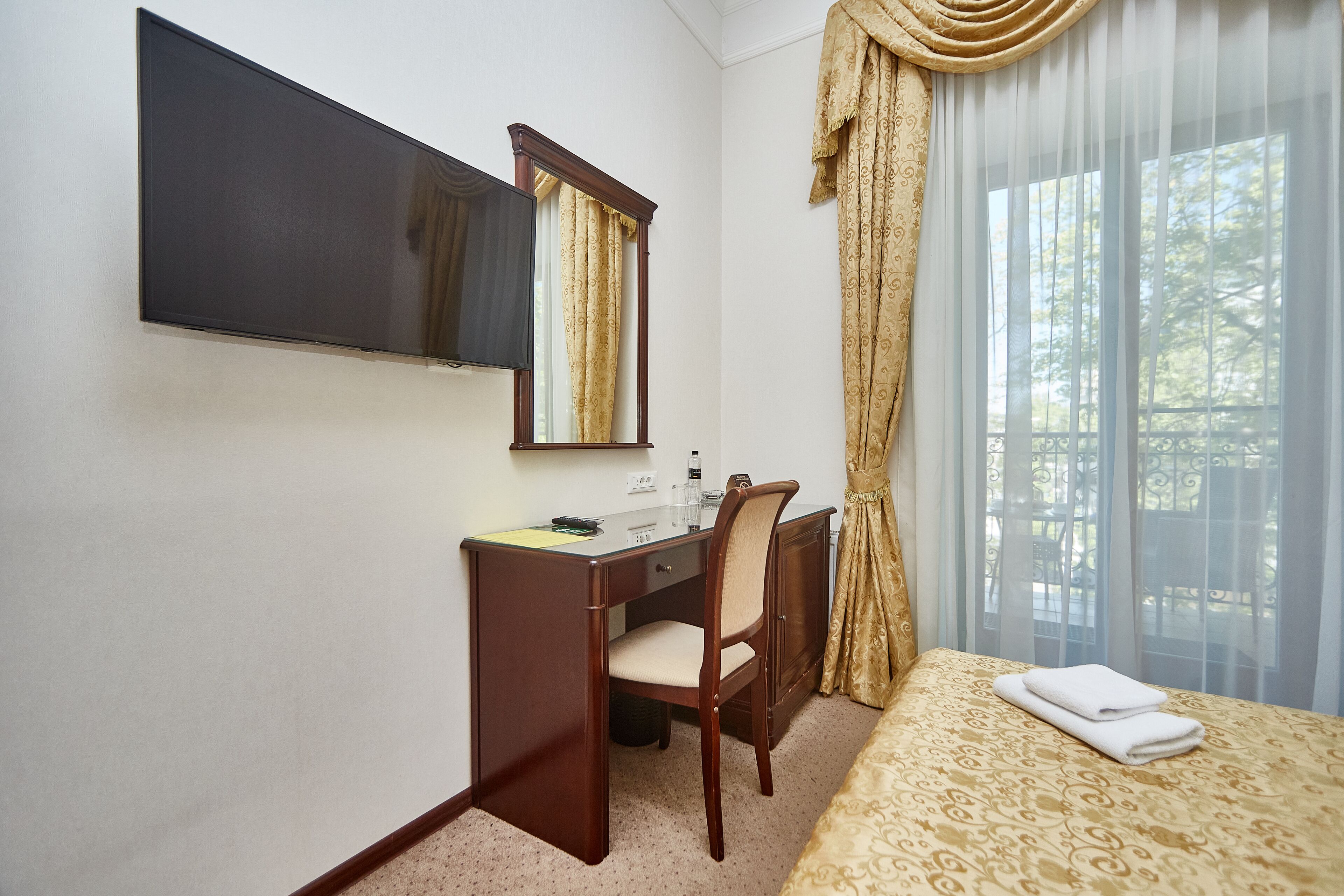 Habitación de hotel con cama, escritorio con silla, televisor de pantalla plana, espejo y ventana con cortinas.
