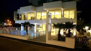 A modern hotel with a pool area, outdoor seating, and a well-lit entrance. - Hotel Fantasy (Riccione)