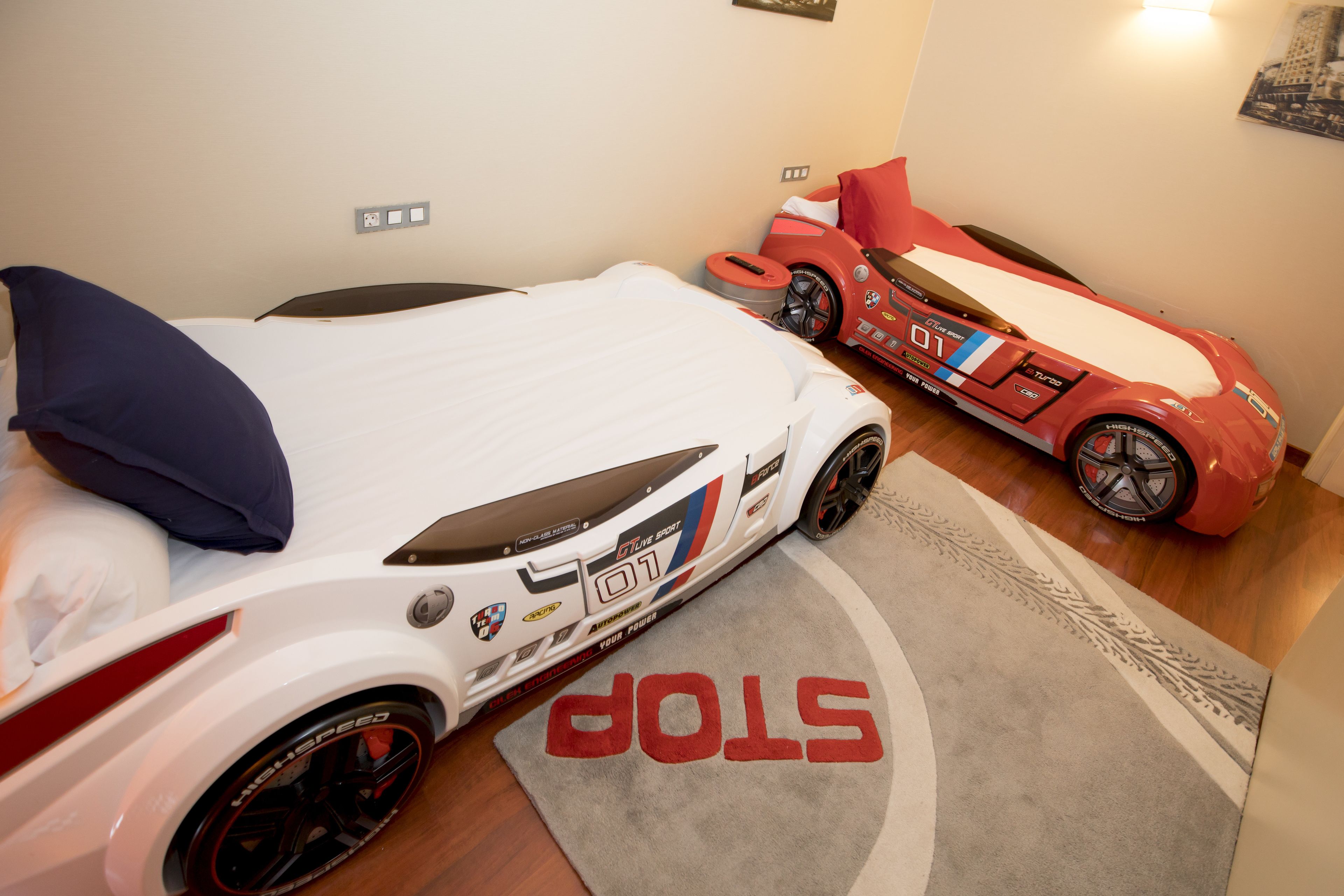 A room with a bed, a red toy car, and a white toy car.