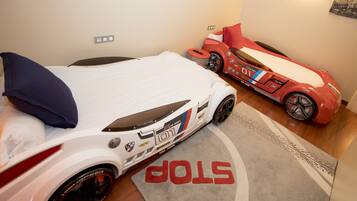 A room with a bed, a red toy car, and a white toy car.