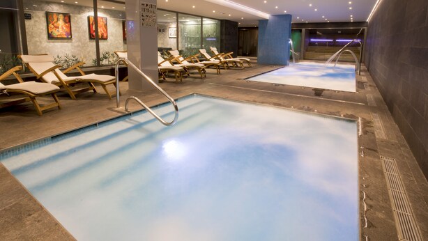 A modern indoor swimming pool with lounge chairs and a glass wall. - Hotel Font d'Argent Canillo (Canillo)