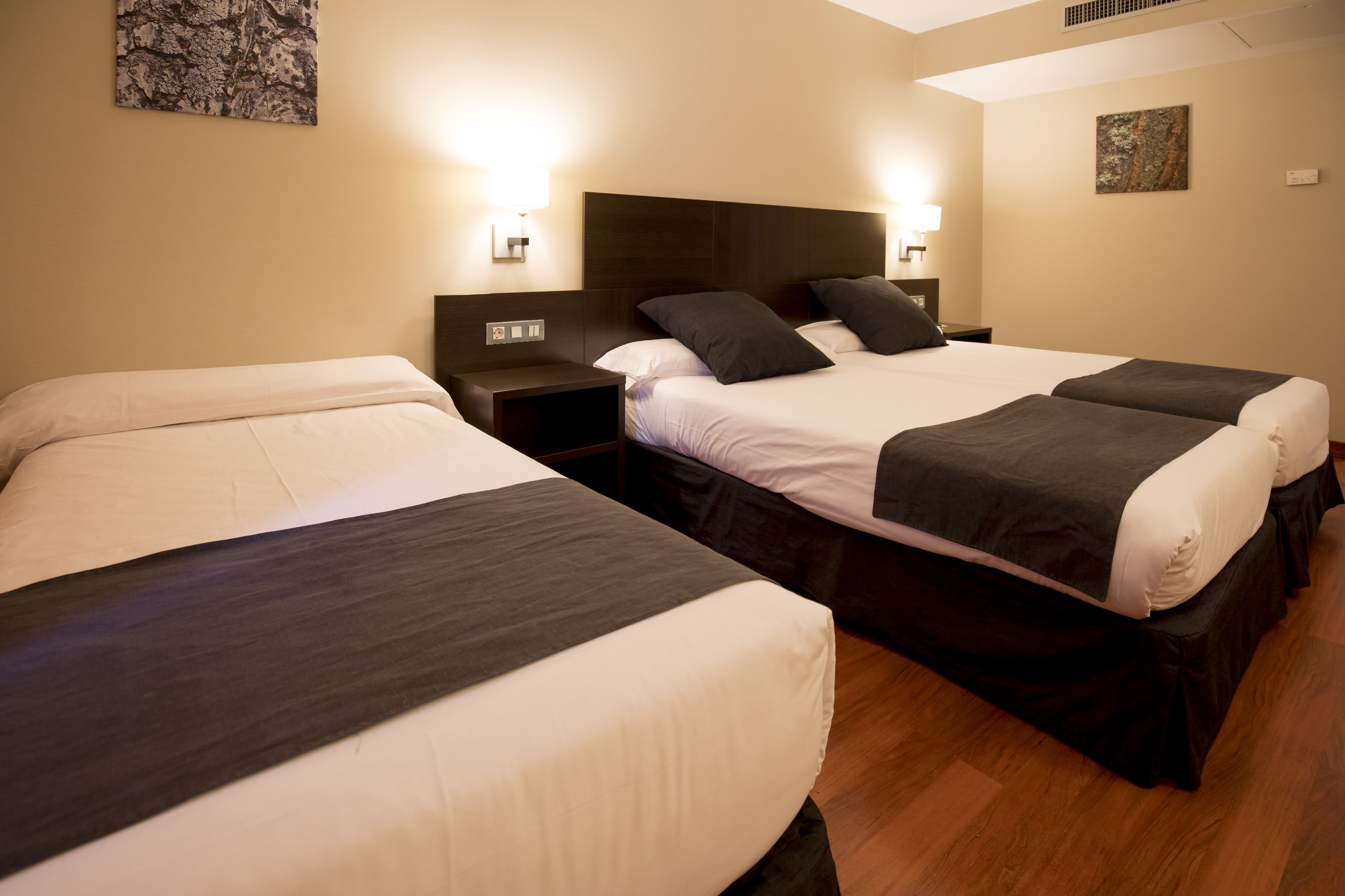 Camera d'albergo con due letti, ognuno con testiera scura e biancheria da letto bianca. Sono presenti comodini con lampade, e il pavimento è in legno.