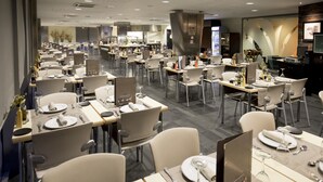 A spacious hotel dining area with multiple tables set for dining, a kitchen in the background, and a modern interior design. - Hotel Font d'Argent Canillo (Canillo)