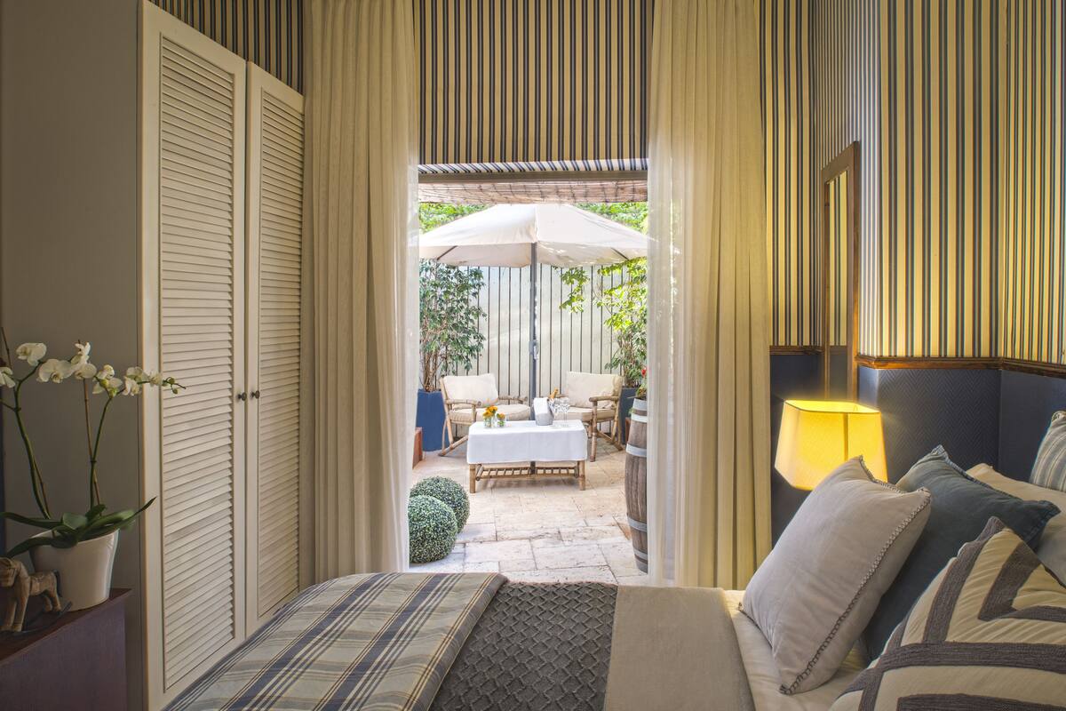 A bedroom with a bed, a nightstand, a lamp, and a view of an outdoor patio with a table and chairs.