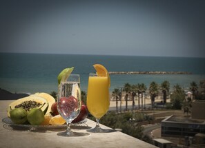 A table with tropical fruits and two glasses of juice, overlooking a beach and ocean. - TLV 88 Sea Hotel (Tel Aviv)
