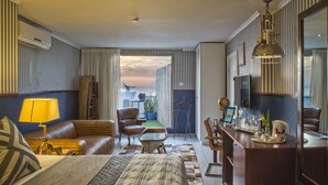 A hotel room with a bed, a desk, a chair, a sofa, a lamp, and a view of the outdoors. - TLV 88 Sea Hotel (Tel Aviv)
