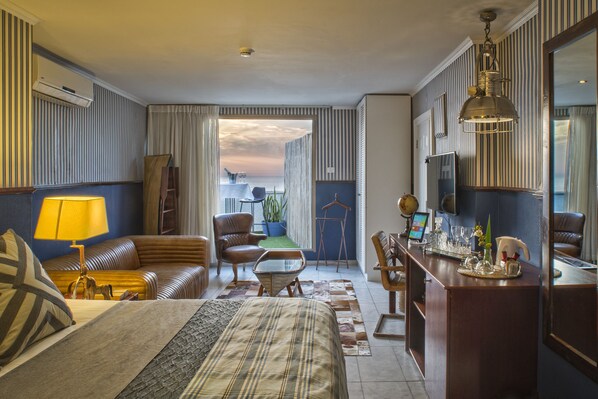 A hotel room with a bed, a desk, a chair, a sofa, a lamp, and a view of the outdoors. - TLV 88 Sea Hotel (Tel Aviv)