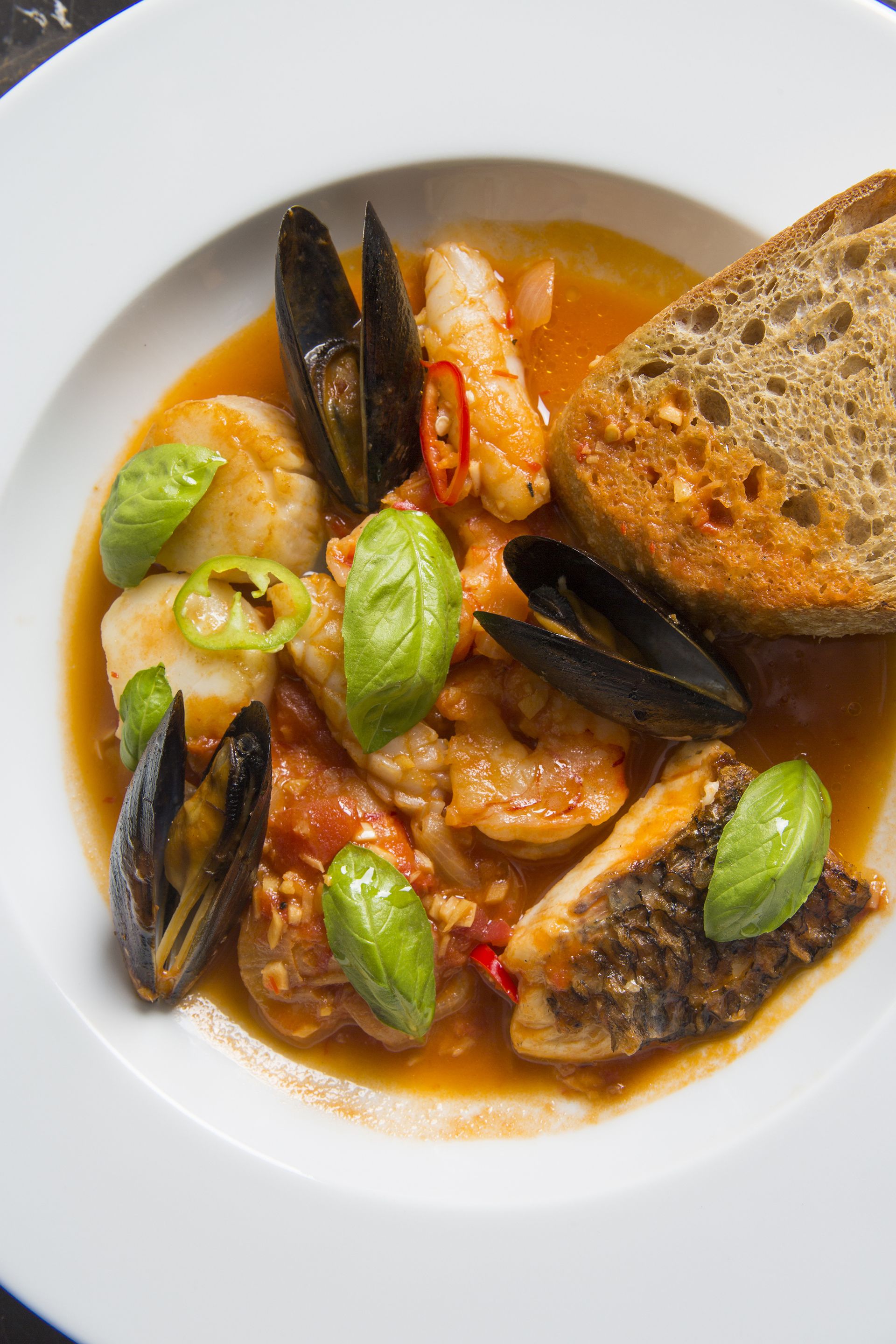 A seafood dish with mussels, shrimp, and bread on a white plate.