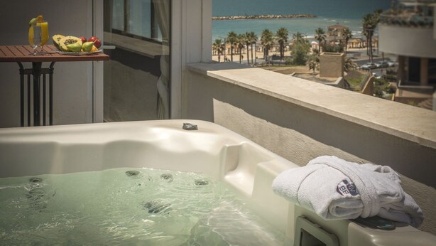 A balcony with a hot tub, a table with fruit and a glass of orange juice, and a view of the beach and ocean. - TLV 88 Sea Hotel (Tel Aviv)