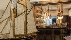 A model ship on a table in a bar area with stools and shelves of bottles in the background. - TLV 88 Sea Hotel (Tel Aviv)