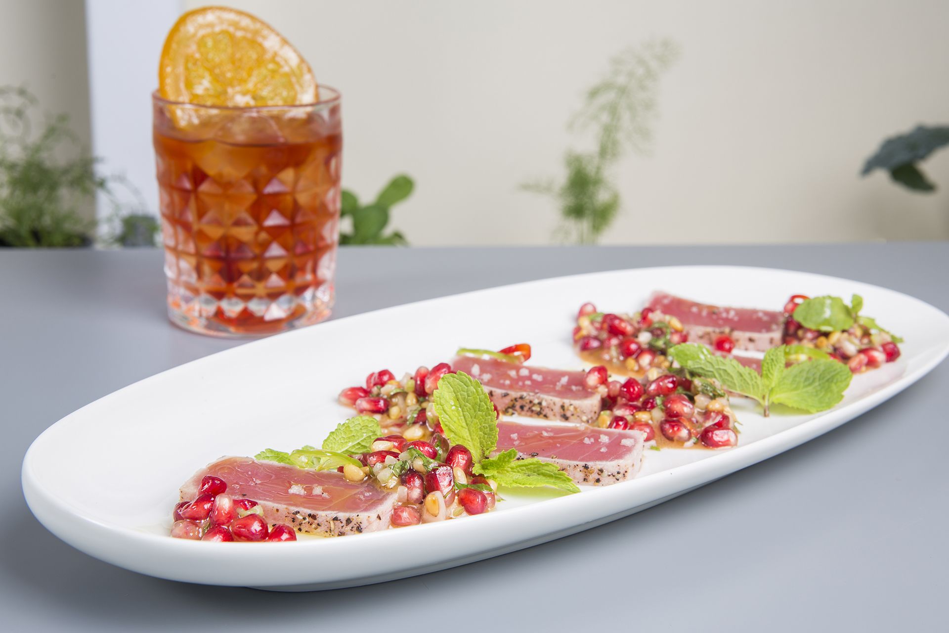 A white plate with slices of cured meat, pomegranate seeds, and mint leaves.