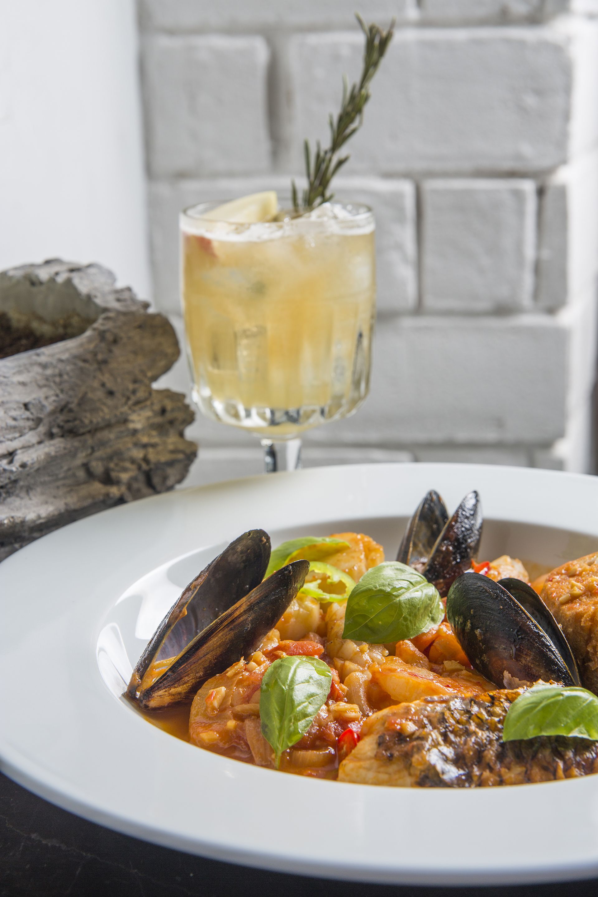Un plat de fruits de mer composé de moules et de basilic, servi sur une assiette blanche, accompagné d’un verre de vin blanc.