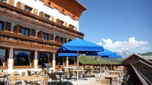 A restaurant with outdoor seating, wooden architecture, and a mountain view. - SportHotel Beausoleil (Huez)