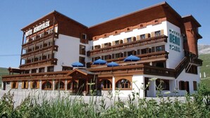 A multi-story hotel with a traditional Alpine architectural style, featuring wooden balconies and a prominent sign. - SportHotel Beausoleil (Huez)