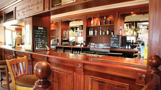 A bar area with wooden furnishings, a chalkboard menu, and a variety of bottles. - SportHotel Beausoleil (Huez)