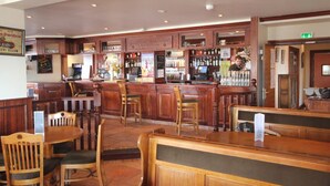 A bar area with wooden furniture, a counter, and various bottles and glasses. - SportHotel Beausoleil (Huez)