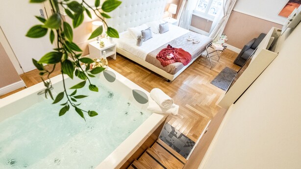 Quarto moderno com uma cama grande, uma mesa de cabeceira, cortinas e uma banheira com uma toalha.