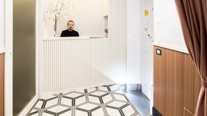 Uma área de recepção com piso de padrão geométrico, um balcão de recepção branco e um lustre no teto.