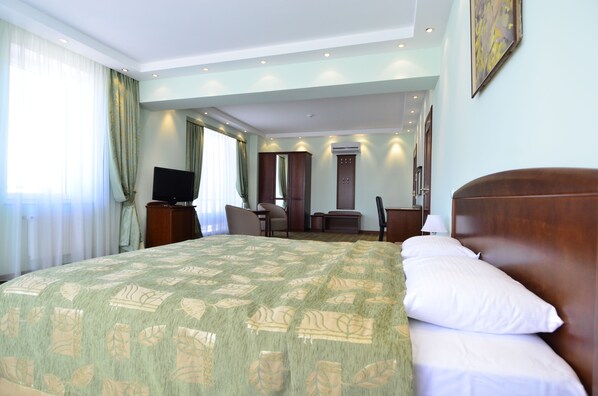 Una habitación de hotel con una cama grande, un escritorio, una silla, un televisor y un armario.