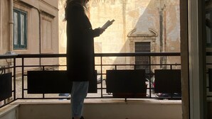 A person standing on a balcony with a view of a building with green domes.