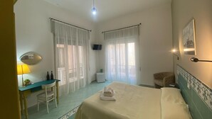 A hotel room with a bed, a desk, a chair, a TV, and a window with curtains.