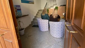 A hallway with a staircase, two patterned ottomans, a potted plant, and a poster on the wall.
