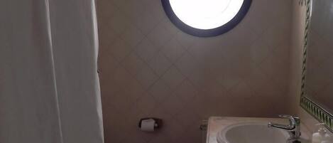 A bathroom with a toilet, sink, and a round mirror with a light above it.