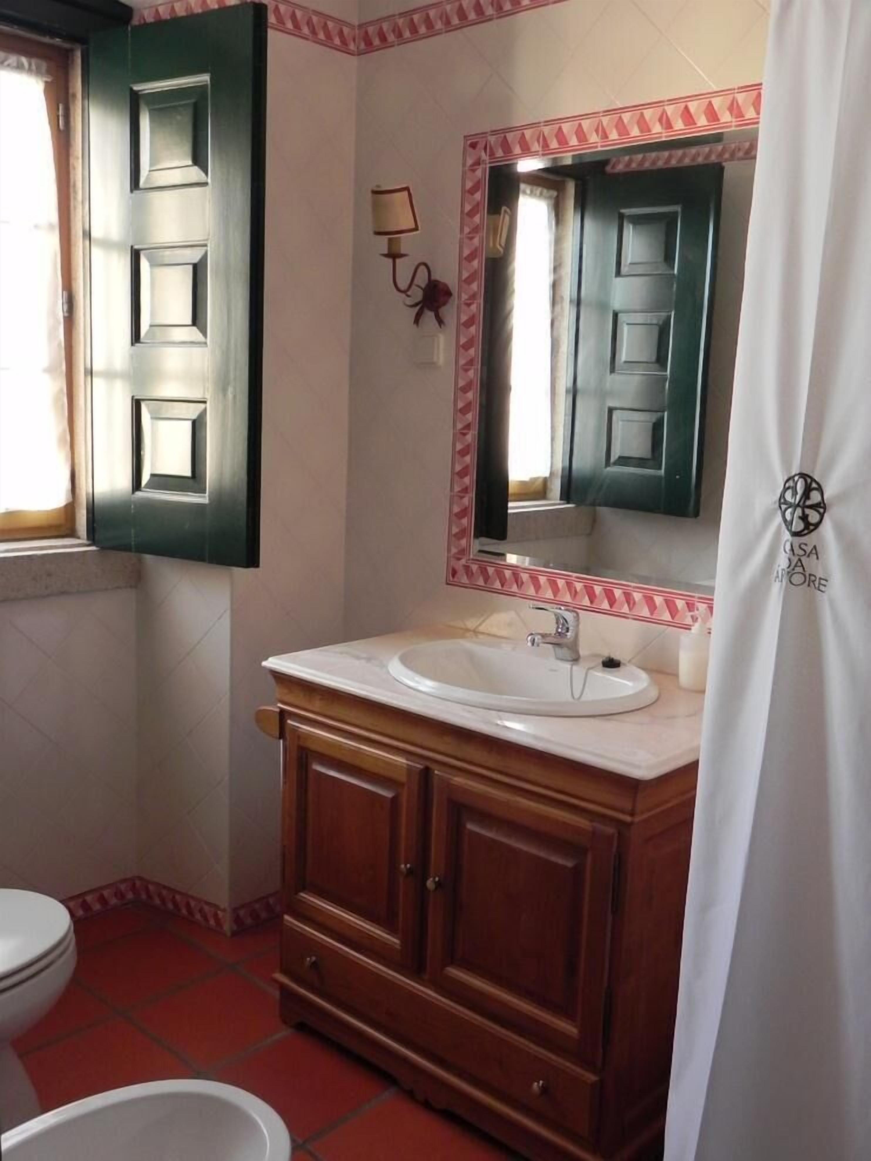 Casa de banho com lavatório branco, toucador de madeira e espelho com moldura decorativa.