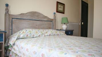 A bedroom with a wooden headboard, floral bedding, a bedside lamp, and a framed picture on the wall.
