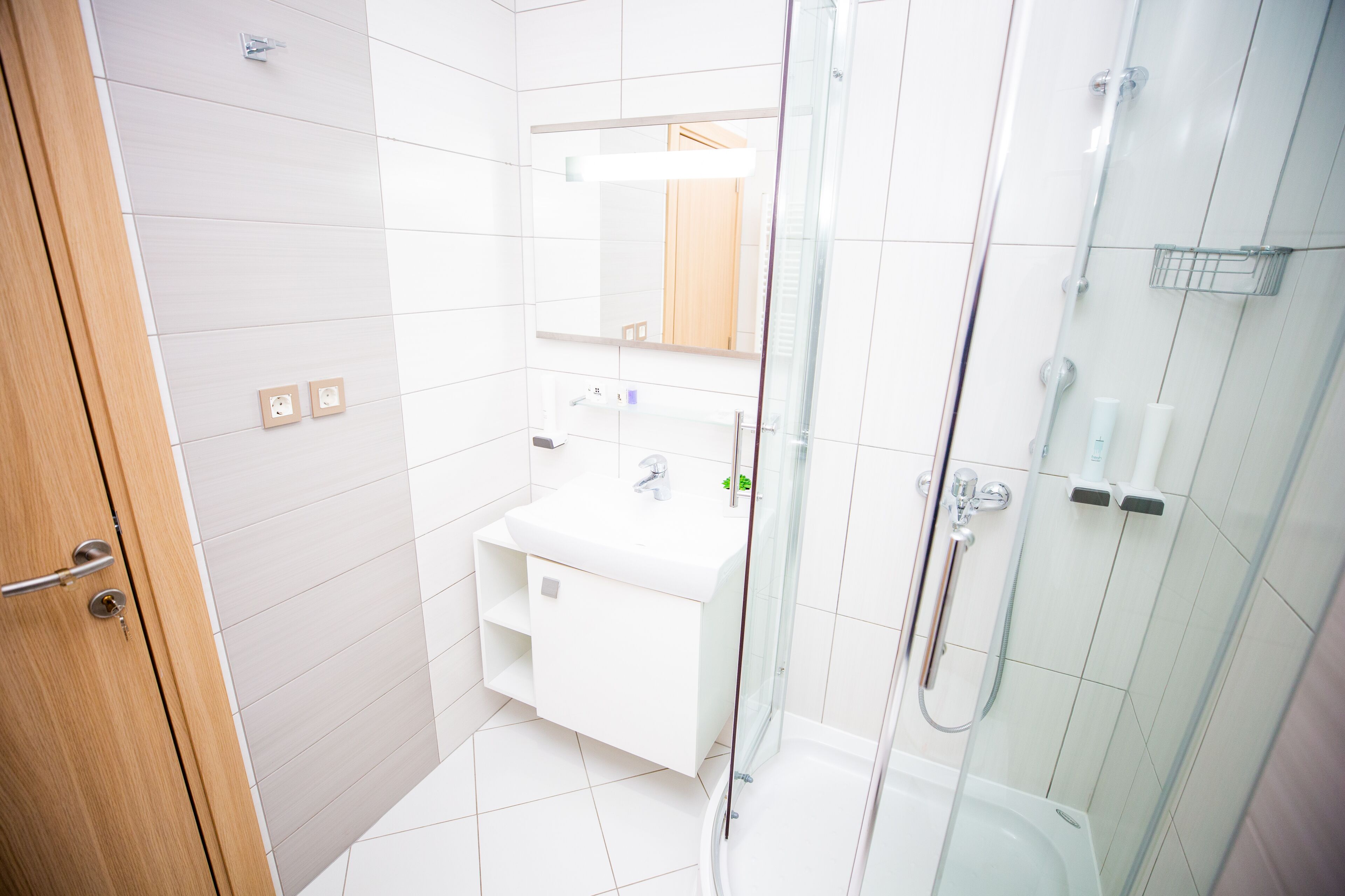 A modern bathroom with a glass shower enclosure, a white sink, and a wooden door.