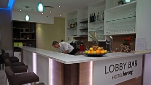 Zona de bar en el vestíbulo, con una barra que muestra un bol de fruta, un cartel que dice 'Lobby Bar Hotelherceg' y un cantinero.