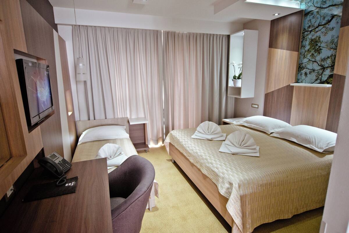 A hotel room with two beds, a desk with a phone, a chair, a TV, and a large window with curtains.