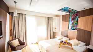 Una habitación de hotel moderna con una cama grande, una zona de estar con una silla, una pequeña mesa con alimentos para el desayuno y un televisor montado en la pared.