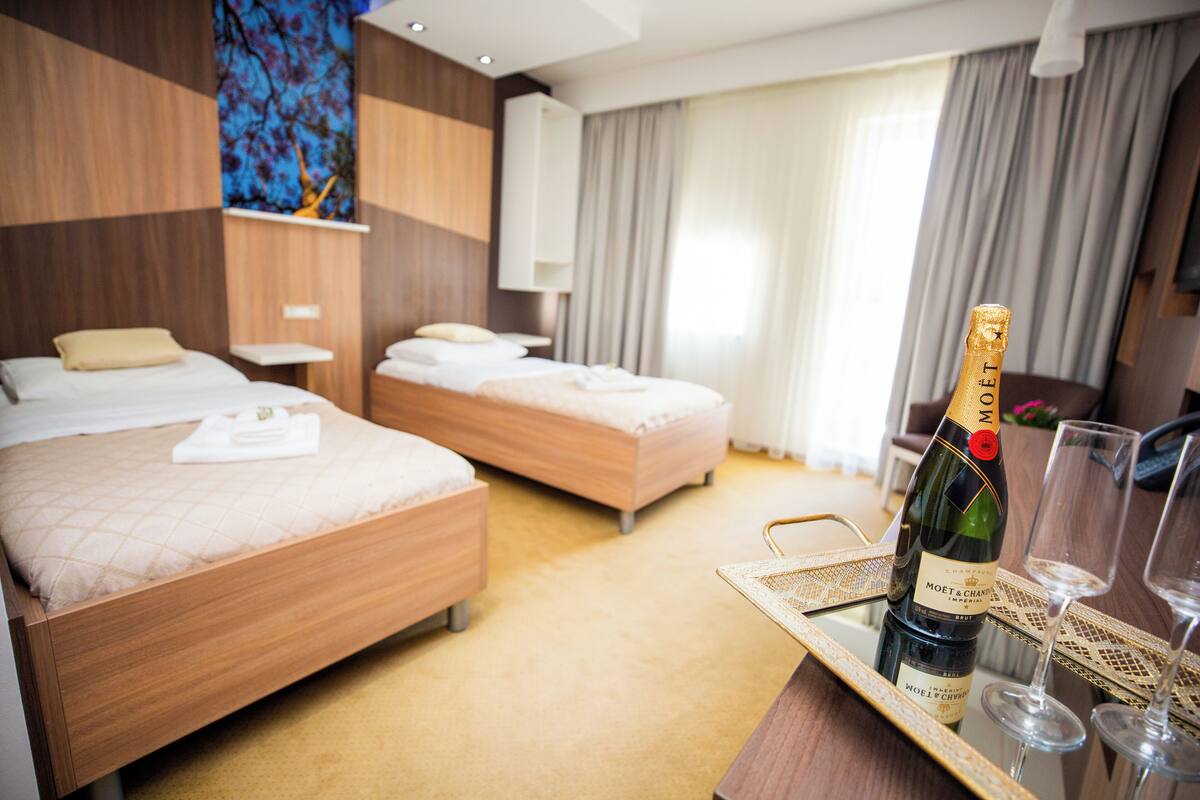 A hotel room with two beds, a minibar, and a bottle of champagne on a tray.