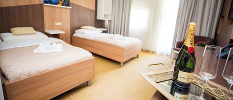 A hotel room with two beds, a minibar, and a bottle of champagne on a tray.