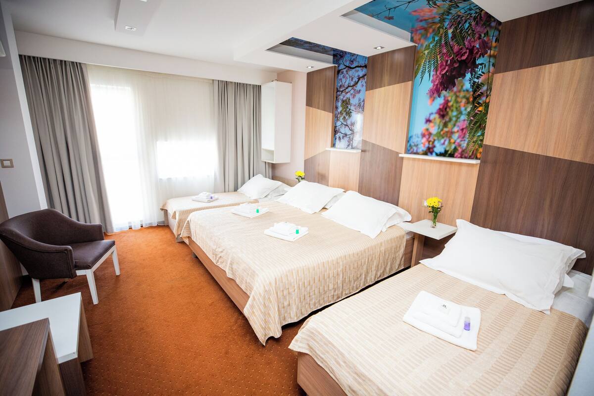 A hotel room with two beds, a desk, a chair, and a large window with curtains.