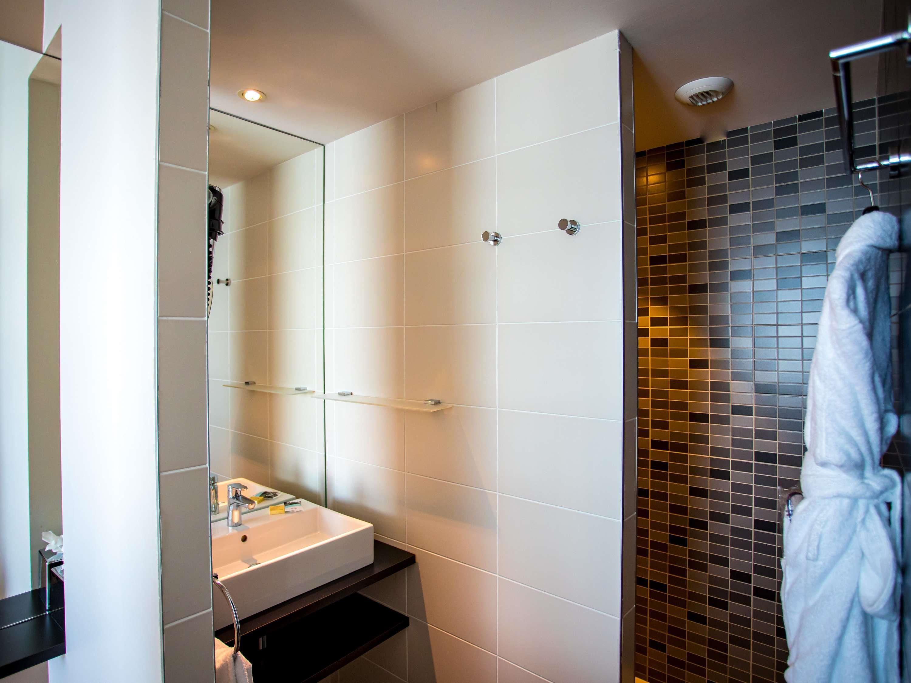 A modern bathroom with a white sink, mirror, and tiled walls.