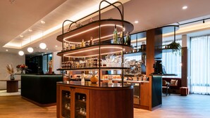 A bar area with a wooden counter, shelves with bottles, and a seating area with a sofa and chairs. - Hotel Mercure Villefranche-sur-Saone (Villefranche-sur-Saône)