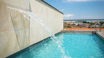 Una piscina con agua cayendo por una pared, rodeada de un suelo de baldosas y un cielo despejado.