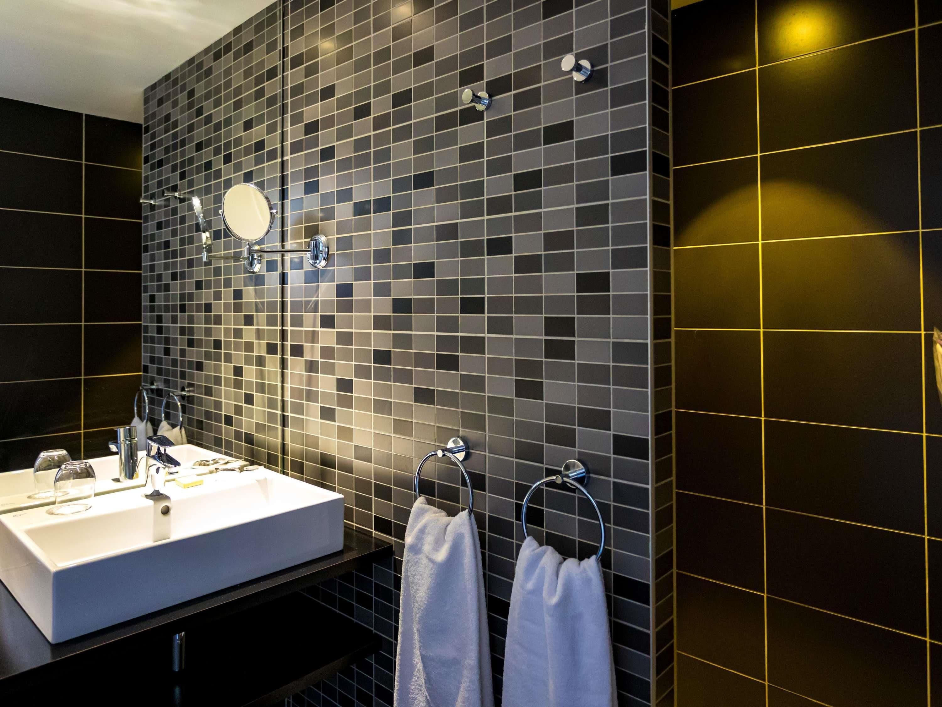 A modern bathroom with a large rectangular sink, a mirror, and two towel rings with white towels.