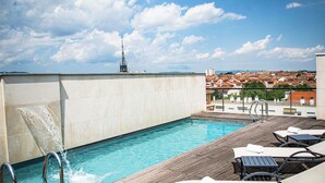 A rooftop pool with a wooden deck, lounge chairs, and a view of a cityscape. - Hotel Mercure Villefranche-sur-Saone (Villefranche-sur-Saône)
