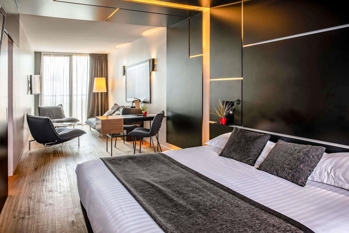 A modern hotel room with a large bed, a desk, and a seating area.