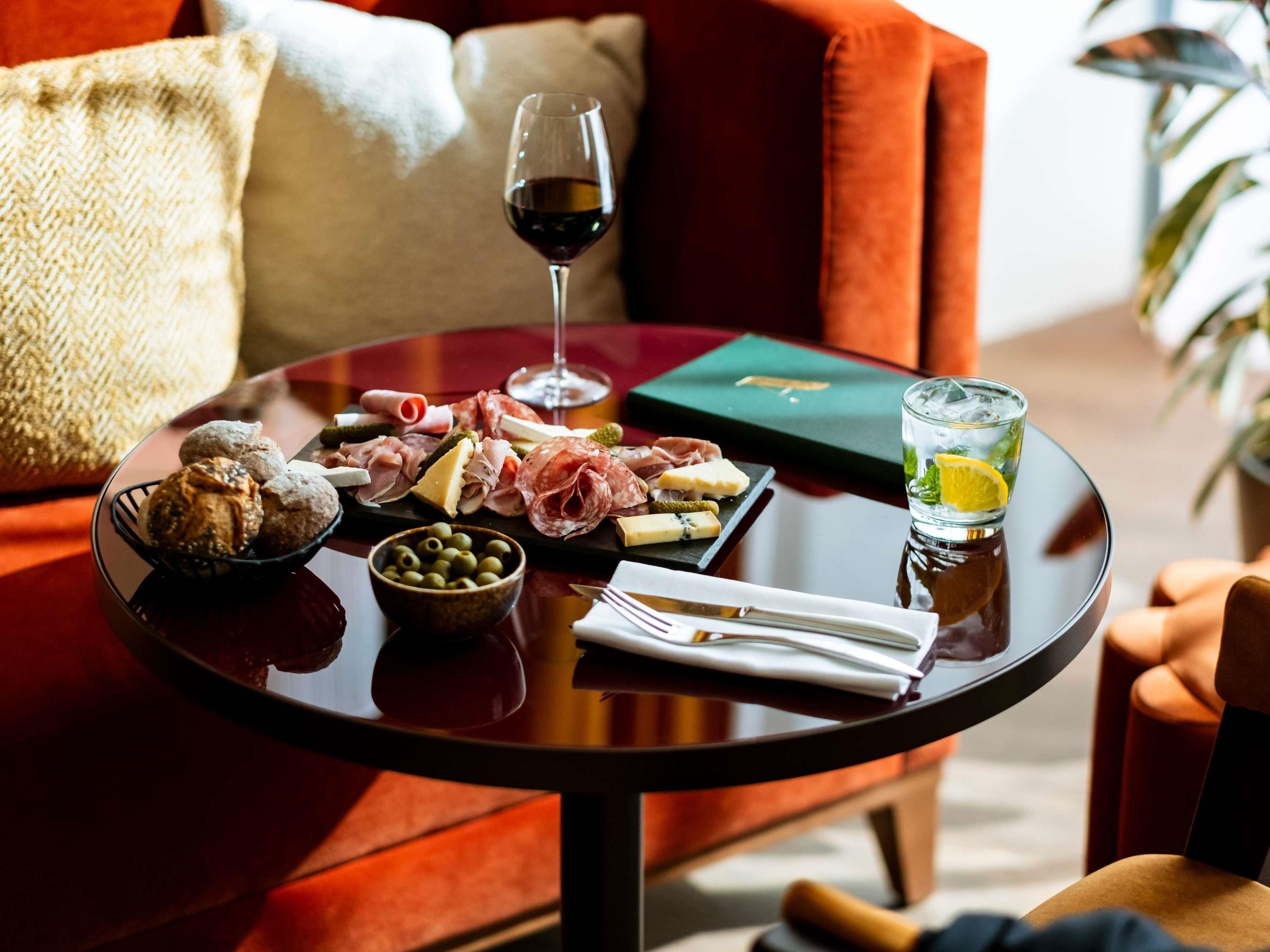 A round table with a variety of cheeses, cured meats, olives, and a glass of red wine.