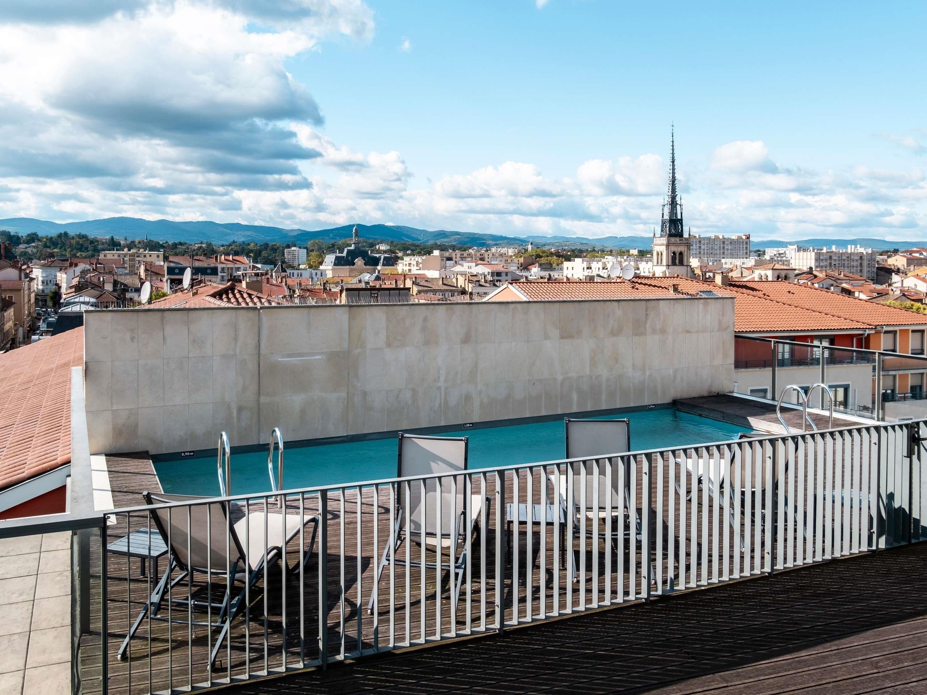 Una piscina en la azotea con vistas a un paisaje urbano, incluyendo una aguja de iglesia.