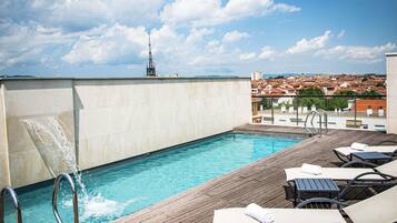 Une piscine sur le toit, avec une terrasse en bois, des chaises longues et une vue sur le paysage urbain.