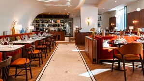 A restaurant with a bar area, wooden tables, and orange seating. - Hotel Mercure Villefranche-sur-Saone (Villefranche-sur-Saône)