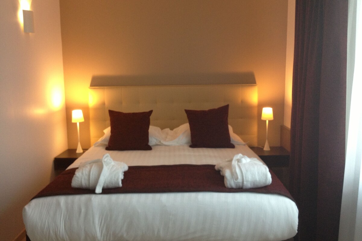 A hotel room with a large bed, two bedside lamps, and a headboard.