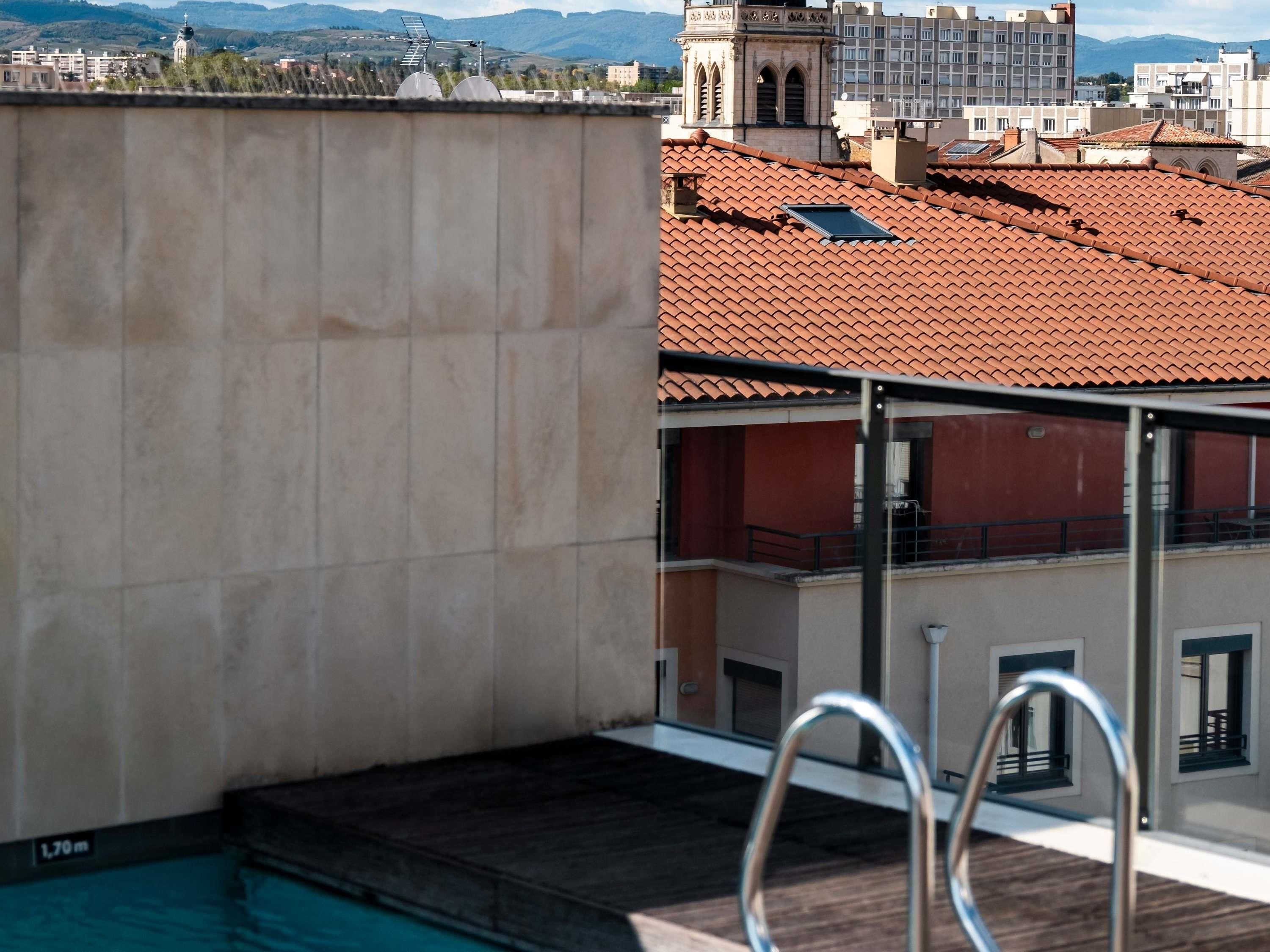 Ein Pool auf dem Dach mit einer Metallleiter, freier Blick auf die Stadt und ein entferntes Gebirge.