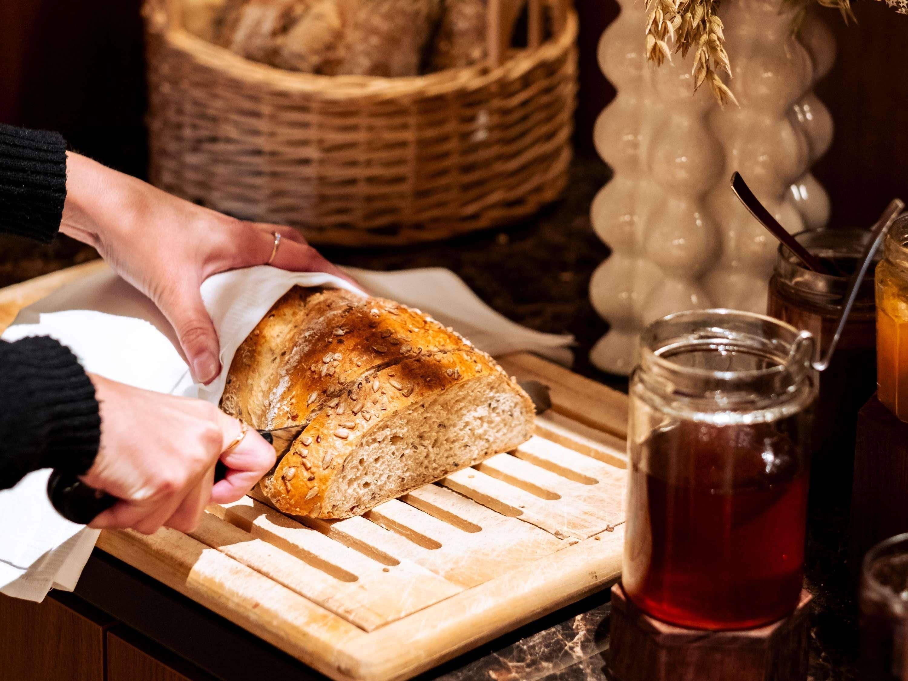 A person cutting a loaf of bread on a wooden cutting board.