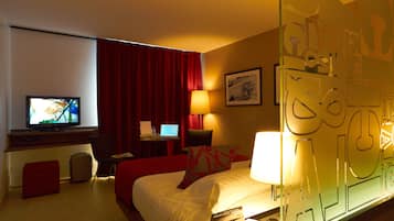 A hotel room with a bed, a desk with a computer, a television, and a red curtain.
